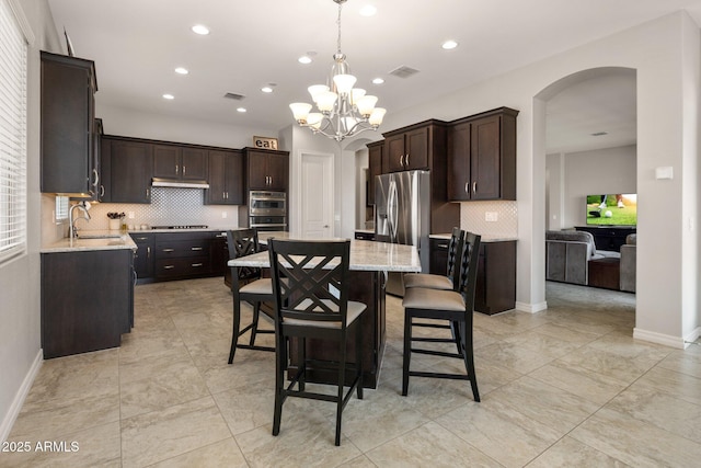 kitchen featuring appliances with stainless steel finishes, a kitchen island, dark brown cabinetry, and under cabinet range hood