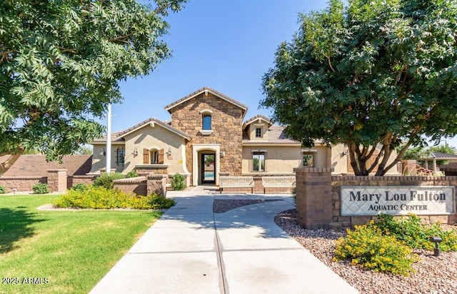 view of front of property featuring fence, stone siding, a tiled roof, stucco siding, and a front lawn