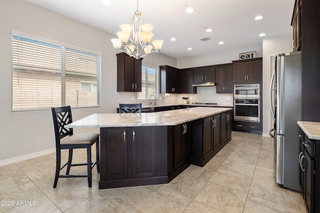 kitchen featuring a kitchen island, freestanding refrigerator, under cabinet range hood, gas cooktop, and backsplash