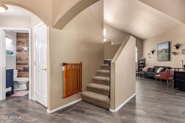 staircase featuring arched walkways, baseboards, and lofted ceiling