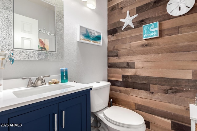bathroom with vanity, a textured wall, toilet, and wooden walls