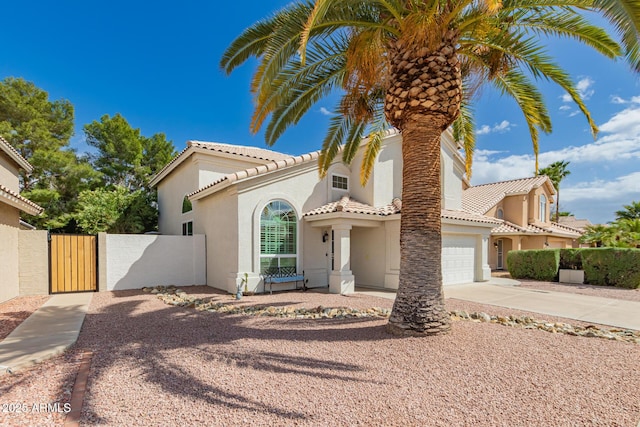 mediterranean / spanish-style house with a gate, fence, a tiled roof, driveway, and stucco siding