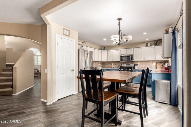 kitchen with appliances with stainless steel finishes, arched walkways, white cabinetry, pendant lighting, and backsplash