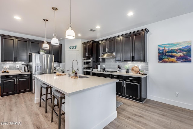 kitchen with sink, hanging light fixtures, a center island with sink, appliances with stainless steel finishes, and a kitchen breakfast bar