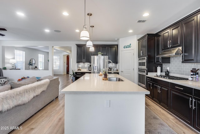 kitchen featuring hanging light fixtures, appliances with stainless steel finishes, a kitchen island with sink, and sink