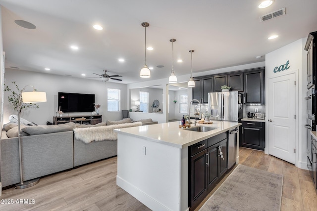 kitchen with pendant lighting, sink, appliances with stainless steel finishes, a kitchen island with sink, and light wood-type flooring