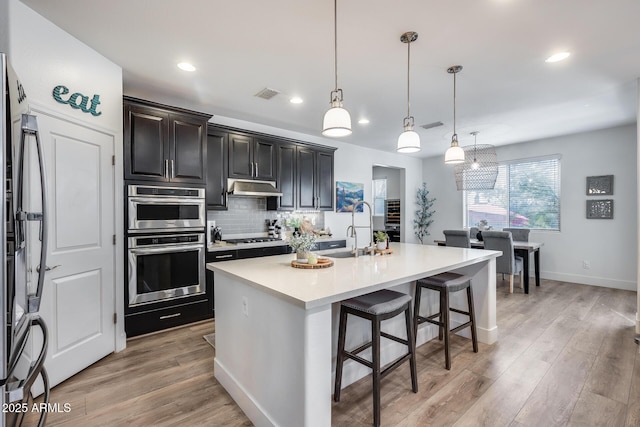 kitchen featuring tasteful backsplash, sink, a kitchen bar, hanging light fixtures, and a center island with sink