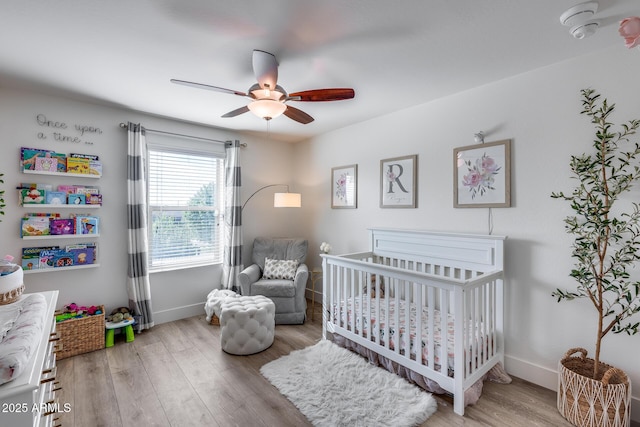 bedroom with a crib, ceiling fan, and light hardwood / wood-style flooring