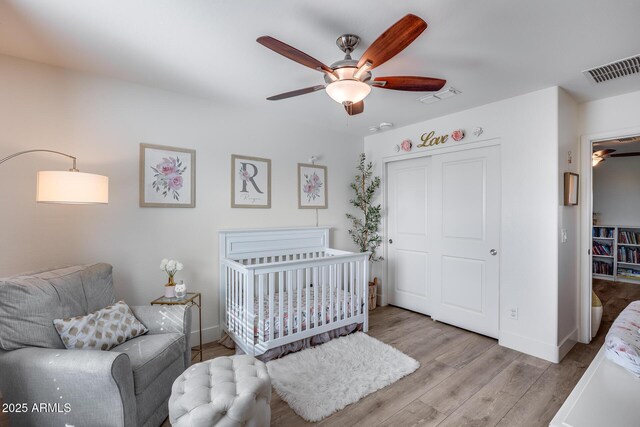 bedroom featuring ceiling fan, light hardwood / wood-style floors, a closet, and a crib