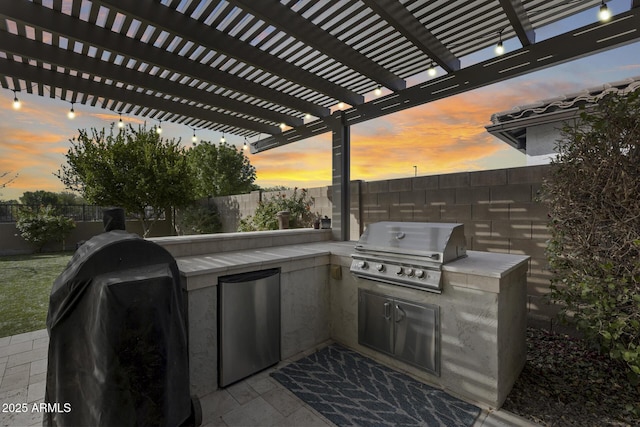 patio terrace at dusk featuring a grill, a pergola, and an outdoor kitchen