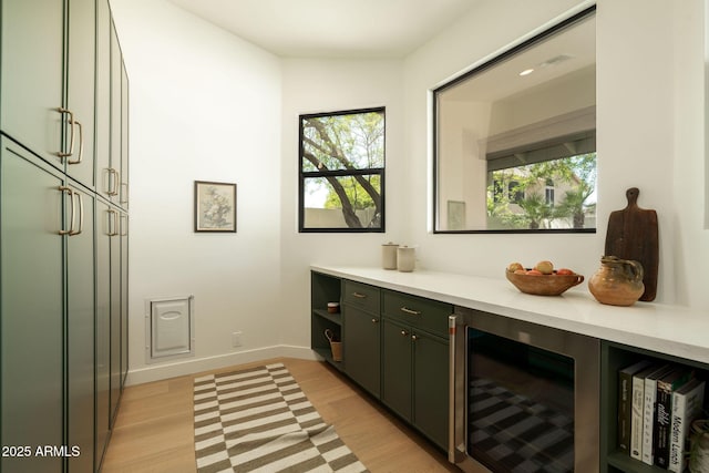 bar with wine cooler, light wood-type flooring, and baseboards
