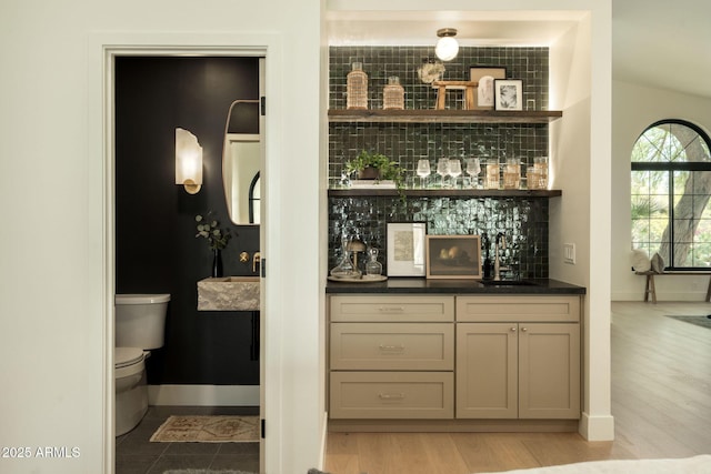 bar featuring light wood finished floors, a sink, tasteful backsplash, baseboards, and a dry bar