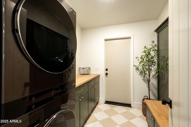 laundry room with stacked washing maching and dryer, light floors, cabinet space, and baseboards
