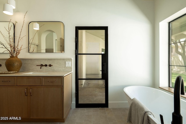 full bathroom featuring a soaking tub, vanity, and baseboards