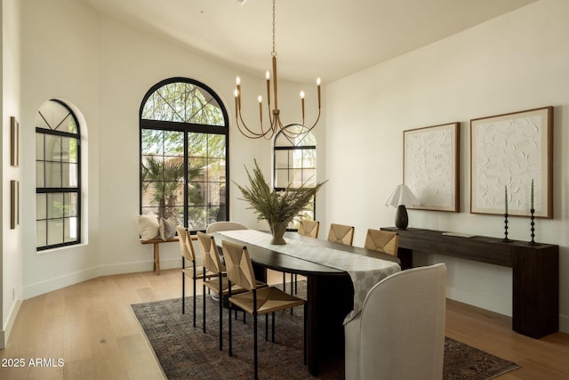 dining room featuring light wood finished floors, high vaulted ceiling, a chandelier, and baseboards