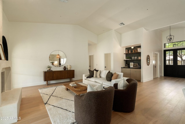 living room with light wood-style floors, high vaulted ceiling, visible vents, baseboards, and a dry bar