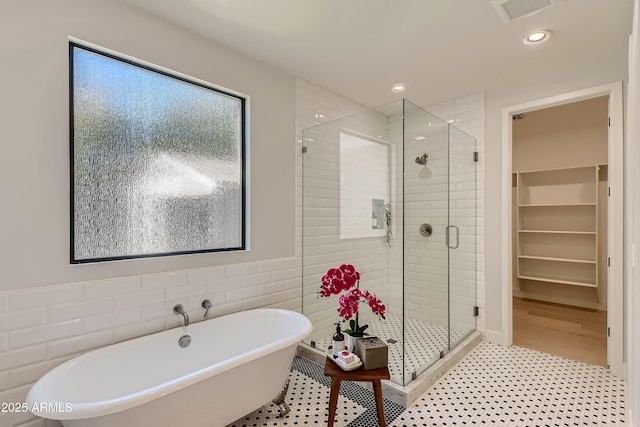 bathroom featuring a walk in closet, tile walls, a shower stall, and a soaking tub