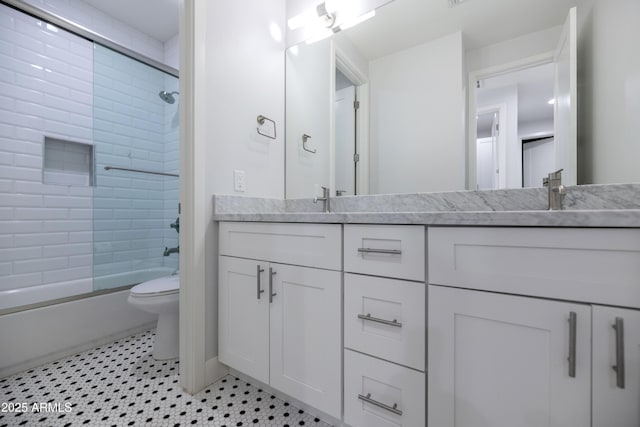 bathroom with double vanity, a sink, combined bath / shower with glass door, and toilet