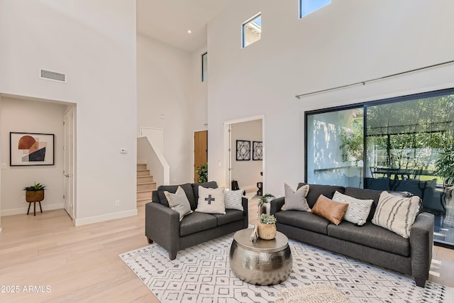 living room with a high ceiling, light wood finished floors, baseboards, visible vents, and stairway