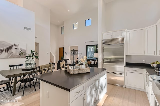 kitchen featuring visible vents, a towering ceiling, dark countertops, light wood finished floors, and stainless steel built in refrigerator