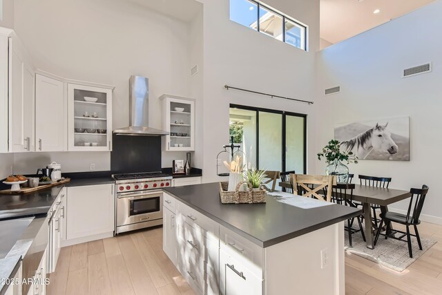 kitchen featuring wall chimney range hood, dark countertops, a high ceiling, visible vents, and premium stove