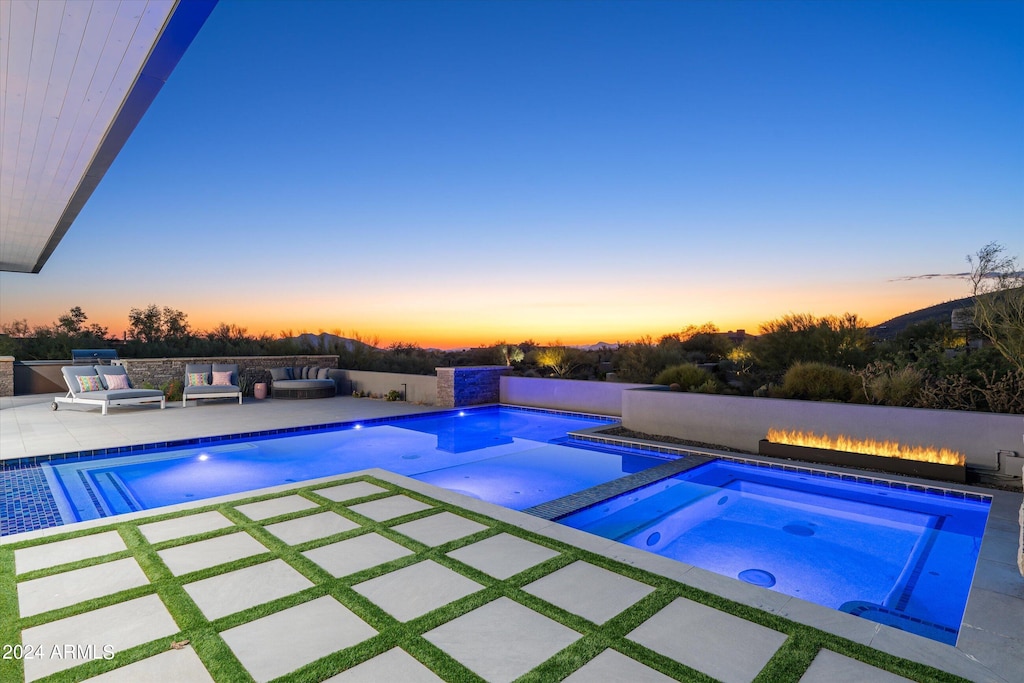 pool at dusk with a patio area and an in ground hot tub