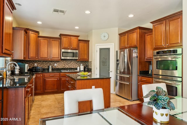 kitchen featuring a sink, a center island, stainless steel appliances, decorative backsplash, and visible vents