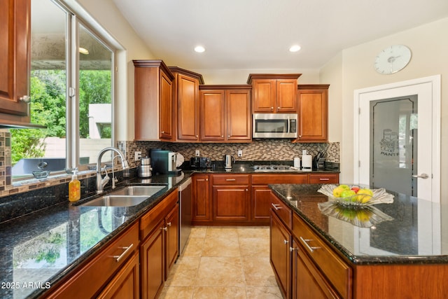 kitchen featuring decorative backsplash, brown cabinets, a sink, dark stone countertops, and appliances with stainless steel finishes