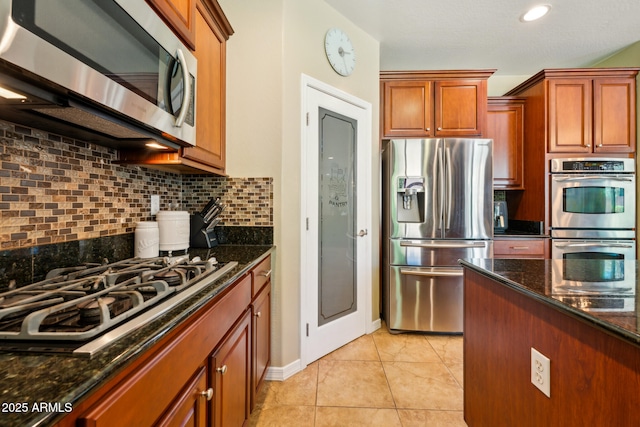 kitchen featuring backsplash, stainless steel appliances, brown cabinetry, and dark stone counters