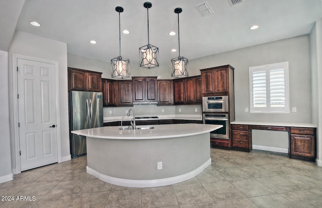 kitchen with a kitchen island with sink, stainless steel appliances, light tile floors, dark brown cabinets, and pendant lighting