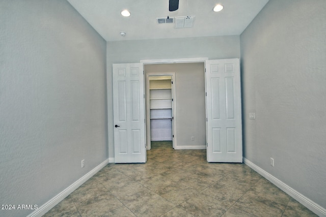 unfurnished bedroom featuring a closet, a spacious closet, dark tile floors, and ceiling fan