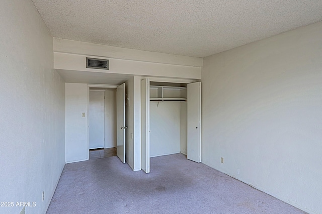 unfurnished bedroom with a closet, visible vents, a textured ceiling, and carpet flooring