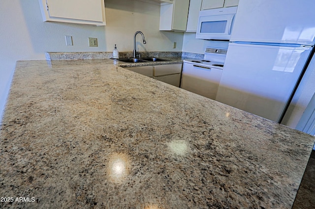 kitchen featuring light stone counters, white appliances, white cabinets, and a sink