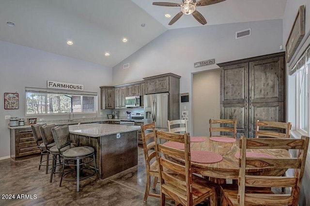 kitchen with a kitchen island, stainless steel appliances, light stone countertops, high vaulted ceiling, and ceiling fan