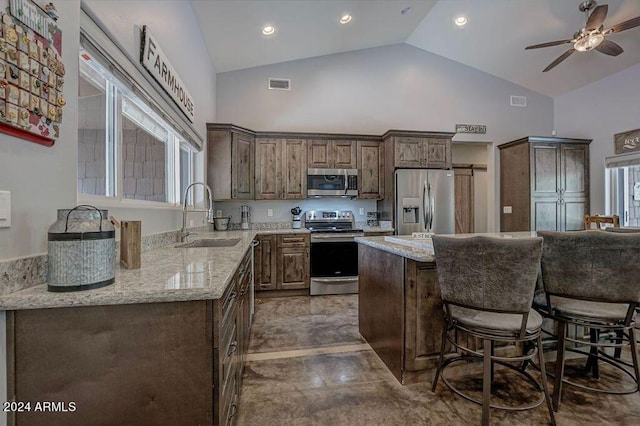 kitchen with high vaulted ceiling, stainless steel appliances, sink, and light stone counters