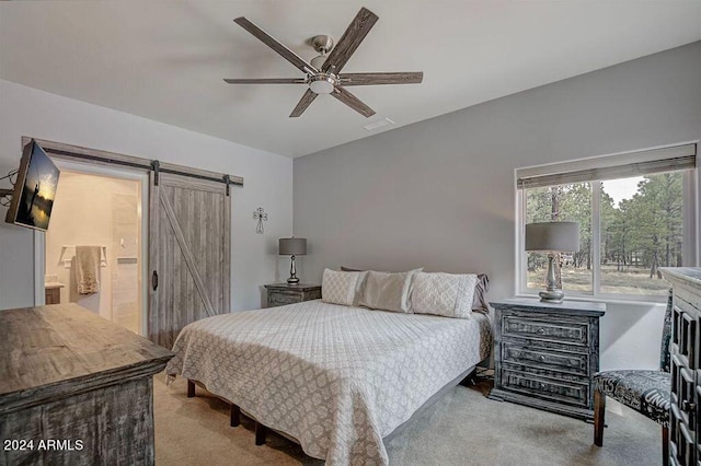 bedroom featuring light carpet, a barn door, ensuite bath, and ceiling fan