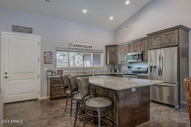 kitchen with light stone counters, a kitchen island, high vaulted ceiling, dark brown cabinetry, and stainless steel appliances