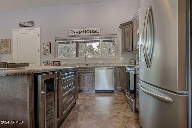 kitchen with appliances with stainless steel finishes, dark brown cabinetry, light stone countertops, and beverage cooler