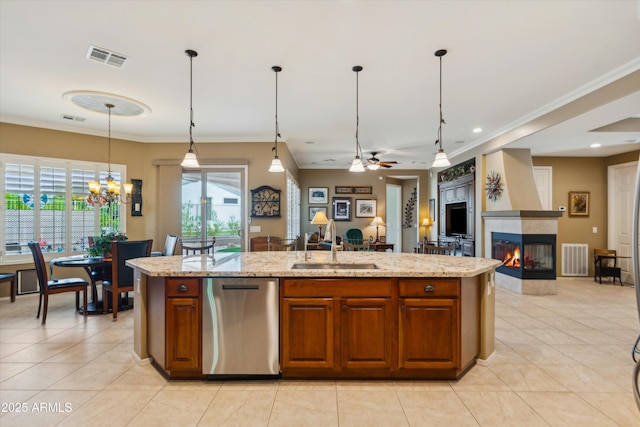 kitchen with a center island with sink, light stone counters, dishwasher, decorative light fixtures, and a tiled fireplace