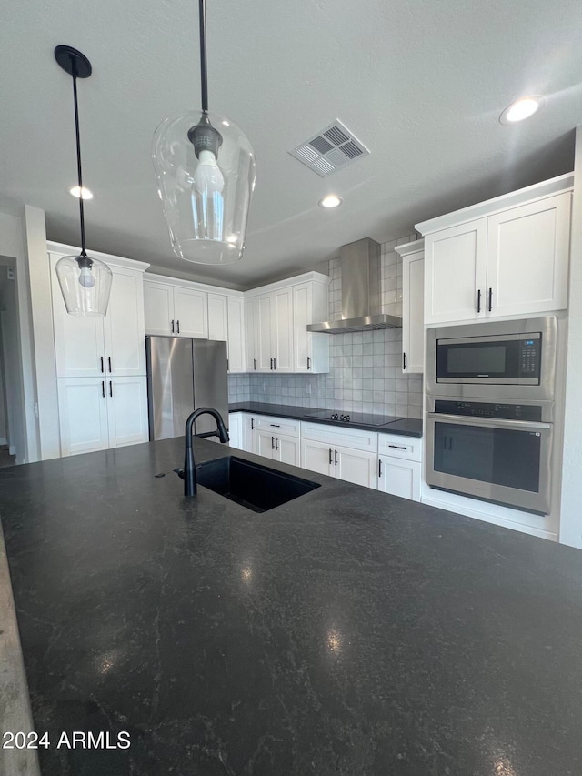 kitchen with appliances with stainless steel finishes, white cabinets, decorative light fixtures, and wall chimney range hood