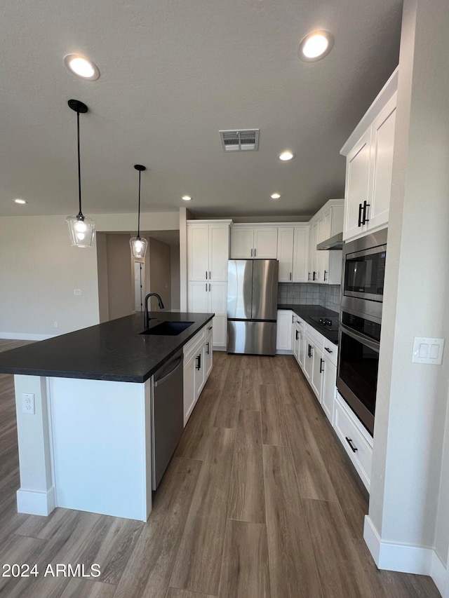 kitchen with a kitchen island with sink, wood-type flooring, decorative light fixtures, white cabinetry, and appliances with stainless steel finishes