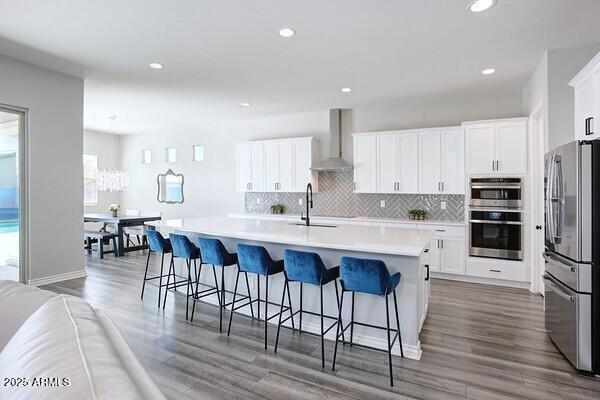 kitchen with light countertops, wall chimney range hood, white cabinets, and stainless steel appliances