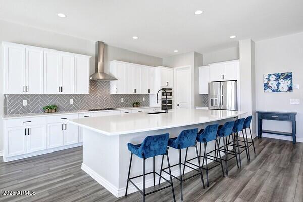 kitchen with a spacious island, white cabinets, stainless steel appliances, and wall chimney exhaust hood