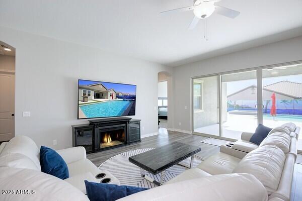 living area featuring a ceiling fan, wood finished floors, a glass covered fireplace, arched walkways, and baseboards