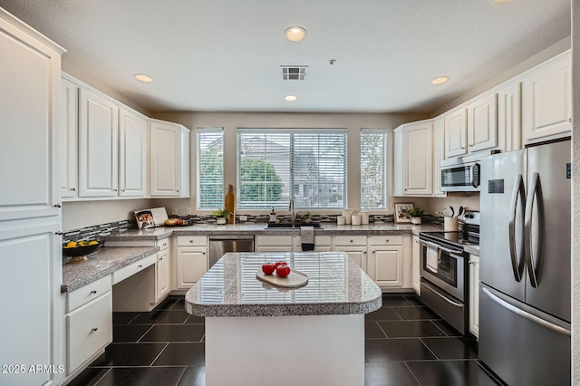 kitchen with visible vents, a center island, dark tile patterned flooring, appliances with stainless steel finishes, and a sink