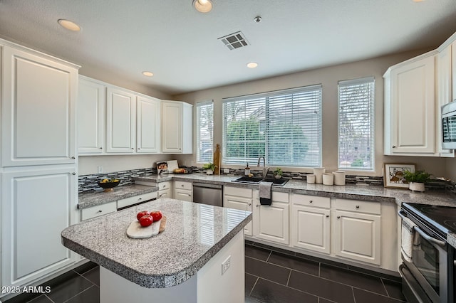 kitchen with visible vents, a sink, white cabinets, stainless steel appliances, and dark tile patterned flooring