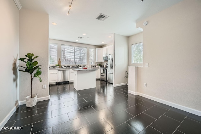 kitchen featuring baseboards, visible vents, stainless steel appliances, white cabinets, and a center island