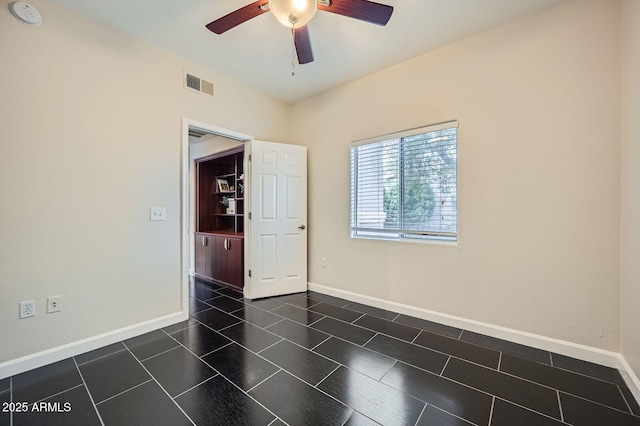 empty room featuring visible vents, baseboards, dark tile patterned flooring, and ceiling fan