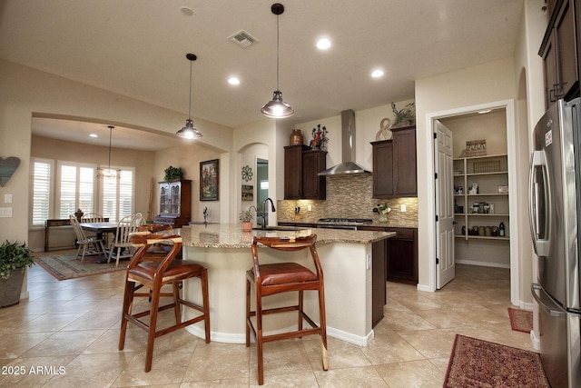 kitchen featuring dark brown cabinets, stainless steel appliances, decorative light fixtures, and wall chimney exhaust hood