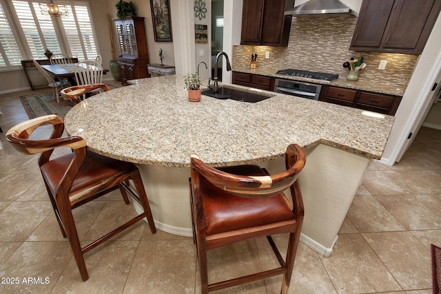 kitchen featuring tasteful backsplash, stainless steel oven, wall chimney range hood, sink, and a breakfast bar area